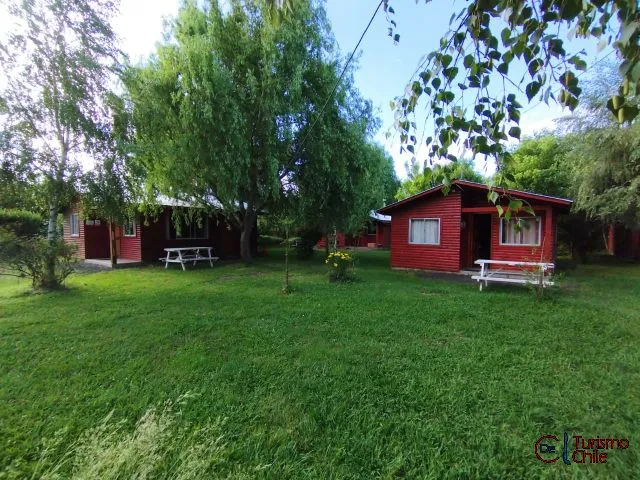 Vista amplia de cabañas rojas con jardines verdes y árboles en Mi Casa
