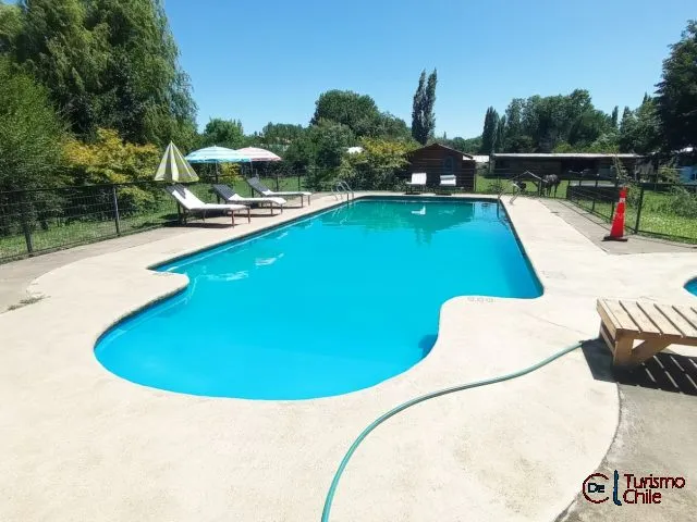 Piscina grande de forma libre con reposeras y sombrillas en Cabañas Mi Casa